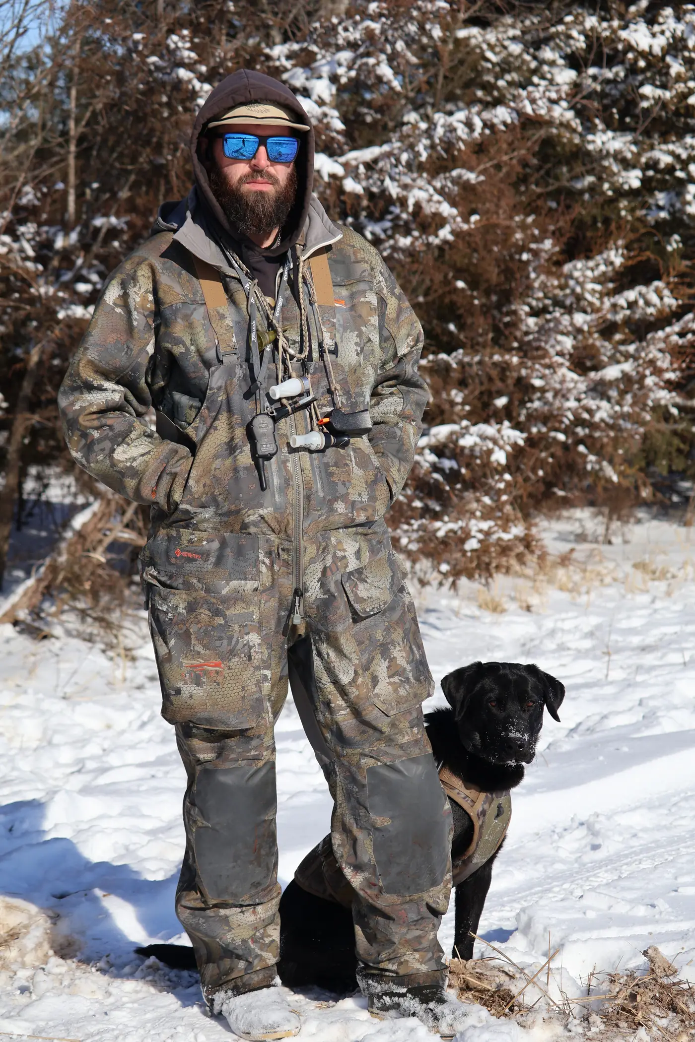 Trey Hubbard, who started Southern Dreams Outdoors, standing in the snow in camo with a black Labrador retriever